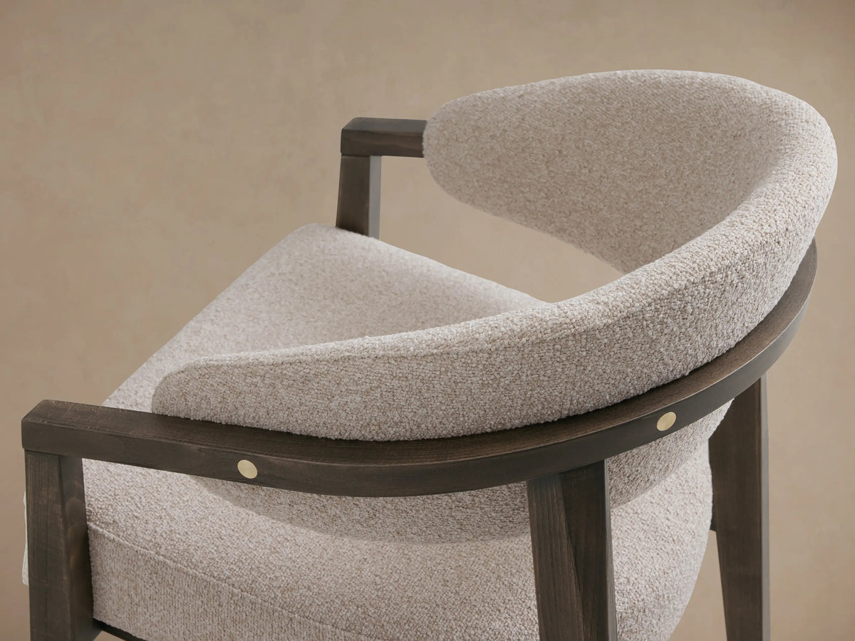 Hagen Dining Chair with light grey padded seat and backrest, featuring dark wood frame with brass button accents, shown at an angle.