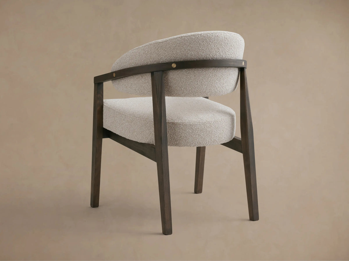 Hagen Dining Chair with solid beech wood frame, curved arms with brass details, light fabric upholstery, and padded seat.
