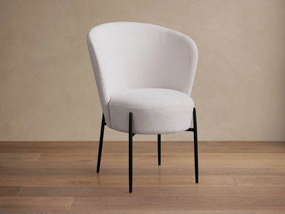Hanne Dining Captain Chair with a rounded white Crypton® fabric seat and back, set on four black metal legs, on a wooden floor.