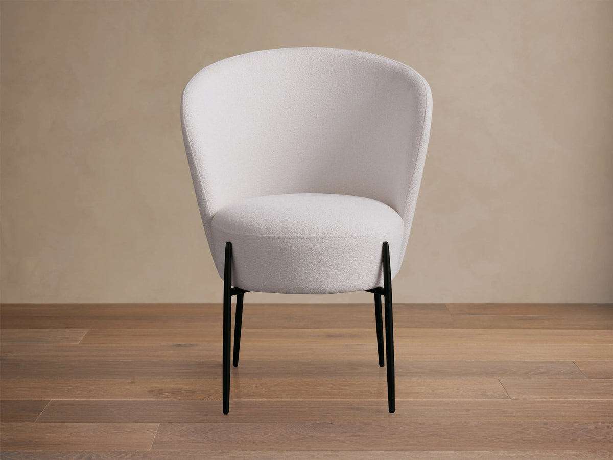 Hanne Dining Captain Chair with a rounded white Crypton® fabric seat and back, set on four black metal legs, on a wooden floor.