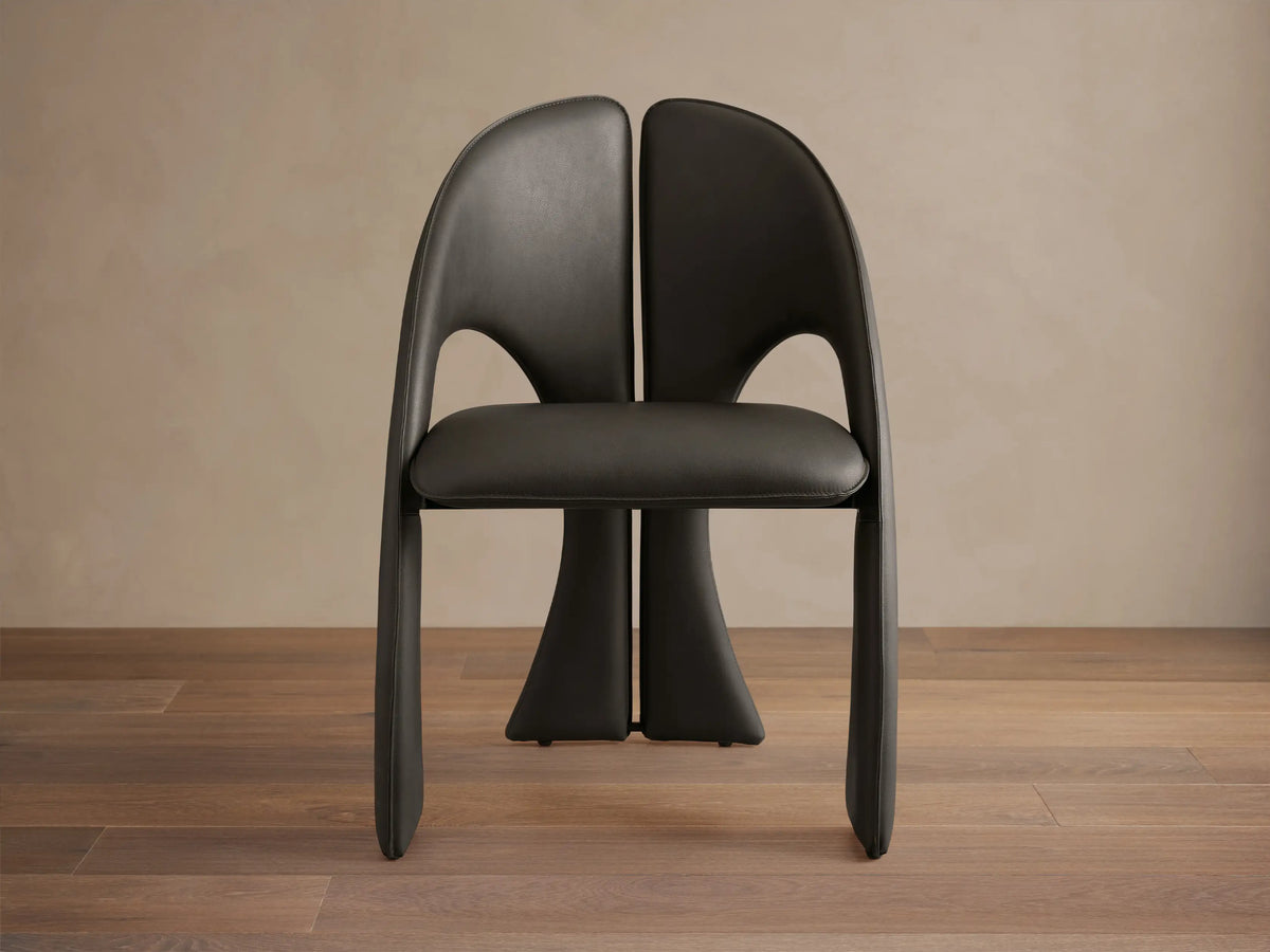 Side profile of a dark gray upholstered Hearst Dining Side Chair with a curved backrest and sculptural, split legs.