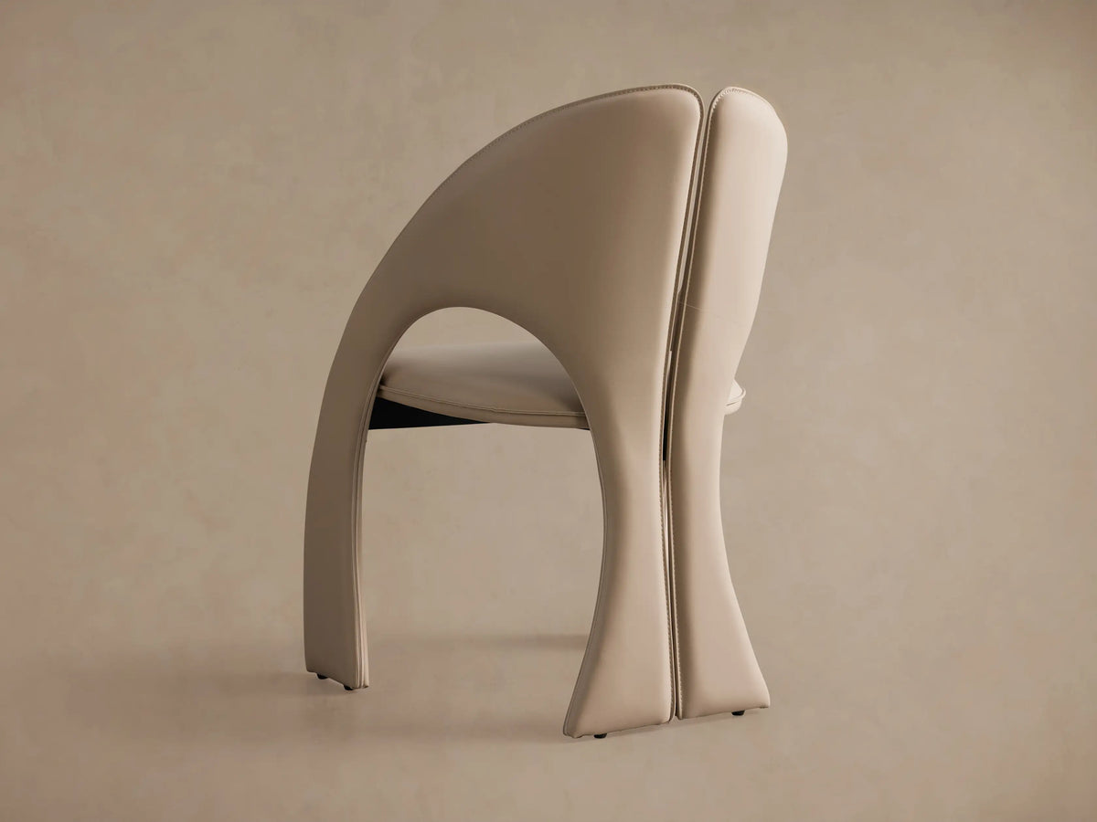 Side profile of the beige Hearst Dining Side Chair with its distinctive curved back, split backrest, and sculptural legs.