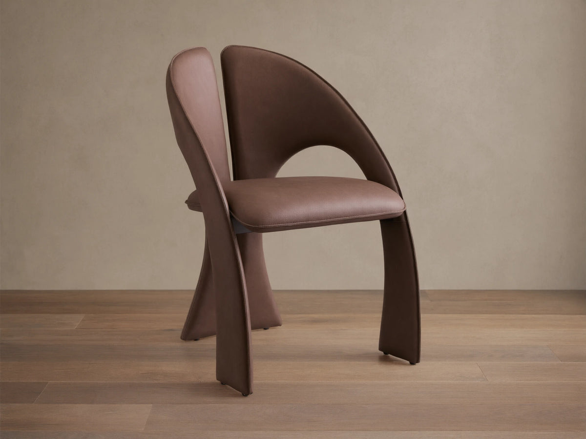 Front view of the brown Hearst Dining Chair, featuring a unique curved upholstered backrest and seat, and distinctive leg design.