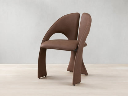 Front view of the brown Hearst Dining Chair, featuring a unique curved upholstered backrest and seat, and distinctive leg design.