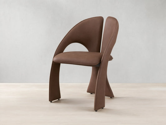Front view of the brown Hearst Dining Chair, featuring a unique curved upholstered backrest and seat, and distinctive leg design.
