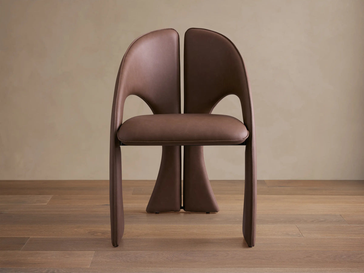 Front view of the brown Hearst Dining Chair, featuring a unique curved upholstered backrest and seat, and distinctive leg design.