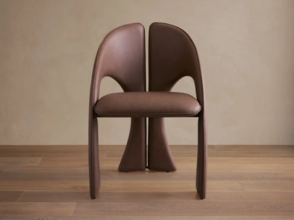 Front view of the brown Hearst Dining Chair, featuring a unique curved upholstered backrest and seat, and distinctive leg design.