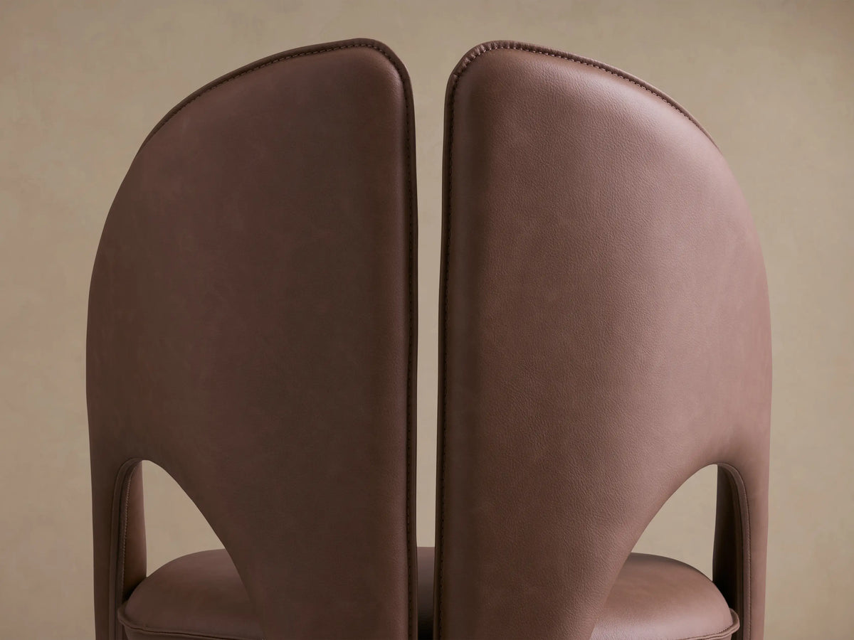 Front view of the brown Hearst Dining Chair, with a distinctive split, curved backrest and upholstered legs.