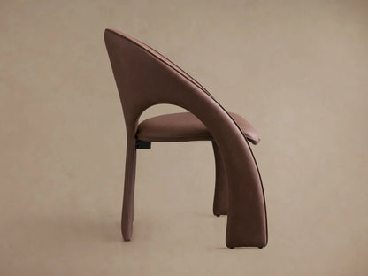Side profile of the taupe upholstered Hearst Dining Chair, with a continuous curved backrest and sculptural flared legs.