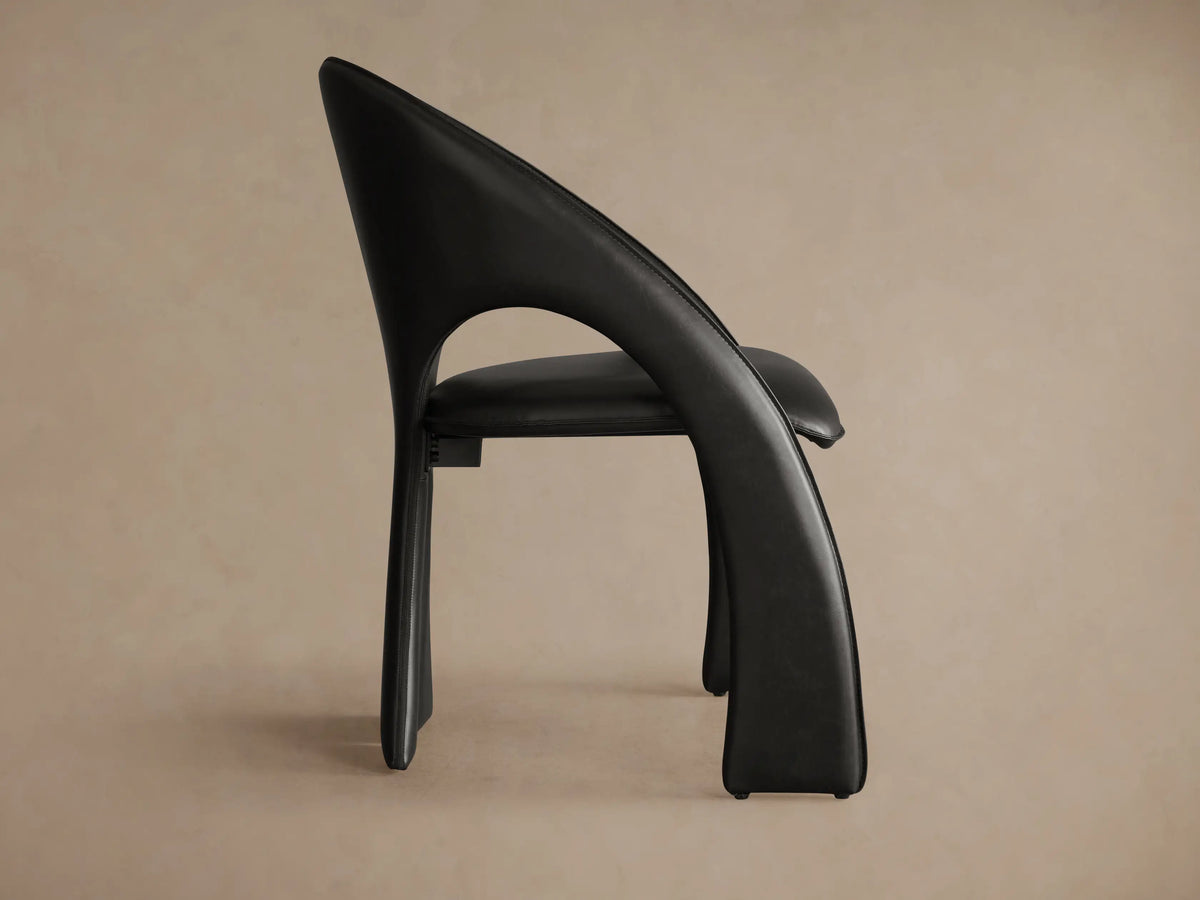 Rear view of the black Hearst Dining Side Chair, showing its gracefully curved back and distinct split, flared legs.