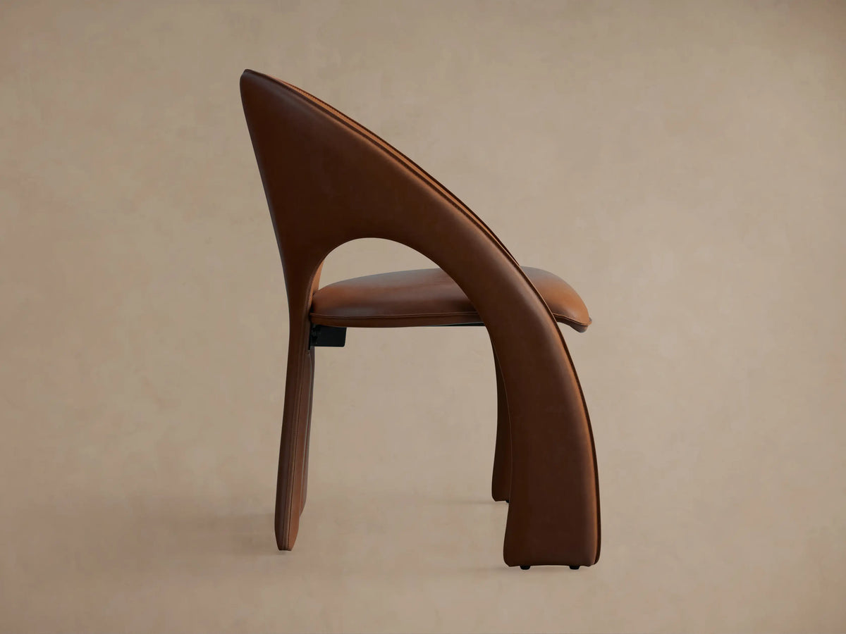 Side view of the brown Hearst Dining Side Chair, showing its upholstered, gracefully curved back and integrated front leg.