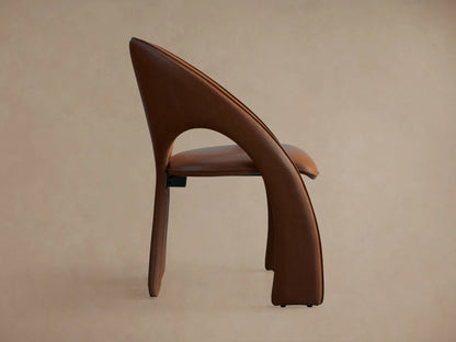 Side view of the brown Hearst Dining Side Chair, showing its upholstered, gracefully curved back and integrated front leg.