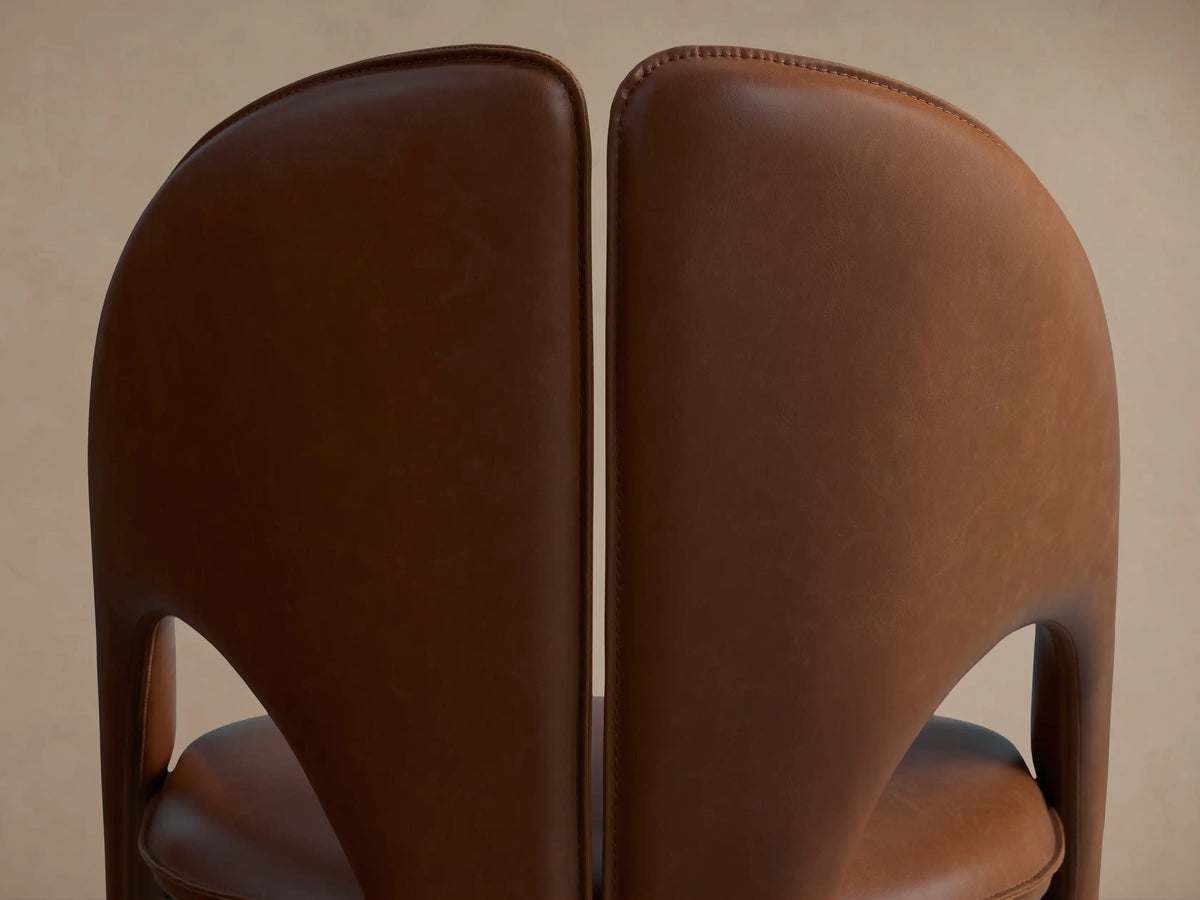 Rear view of a dark brown Hearst Dining Side Chair next to a cognac brown Hearst Dining Side Chair, showing curved leather backs.