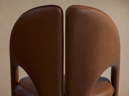 Rear view of a dark brown Hearst Dining Side Chair next to a cognac brown Hearst Dining Side Chair, showing curved leather backs.