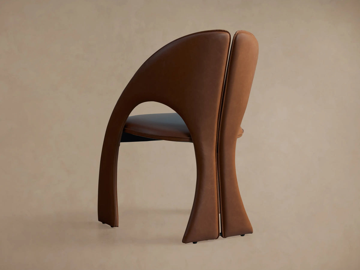 Side profile of the brown Hearst Dining Side Chair, showing its curved upholstered back, split design, and dark seat cushion.
