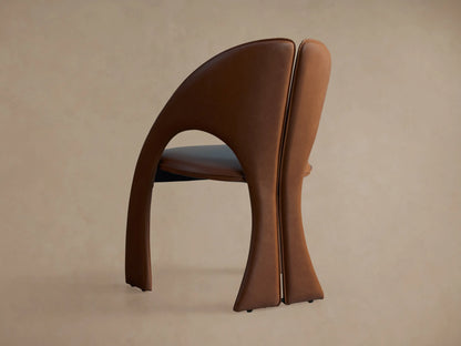 Side profile of the brown Hearst Dining Side Chair, showing its curved upholstered back, split design, and dark seat cushion.