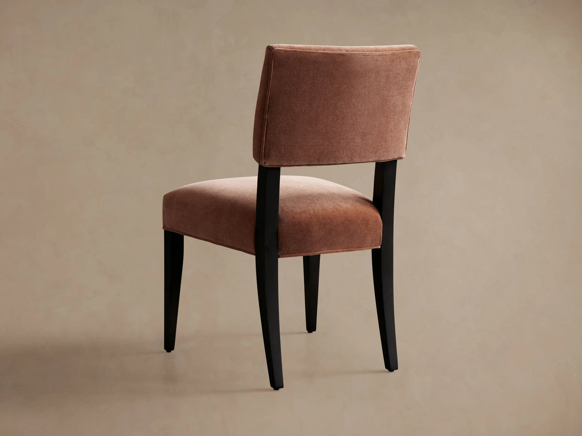 Hartley Dining Chair: close-up of salmon-colored velvet upholstered backrest and seat on a dark wood frame.