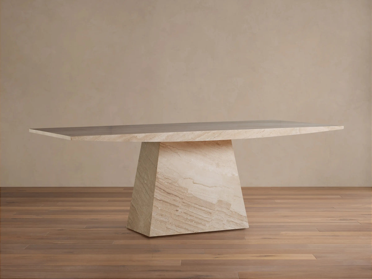 Ilaria Dining Table, crafted from honed beige coralle marble. It has a long rectangular top & a thick, trapezoidal base.