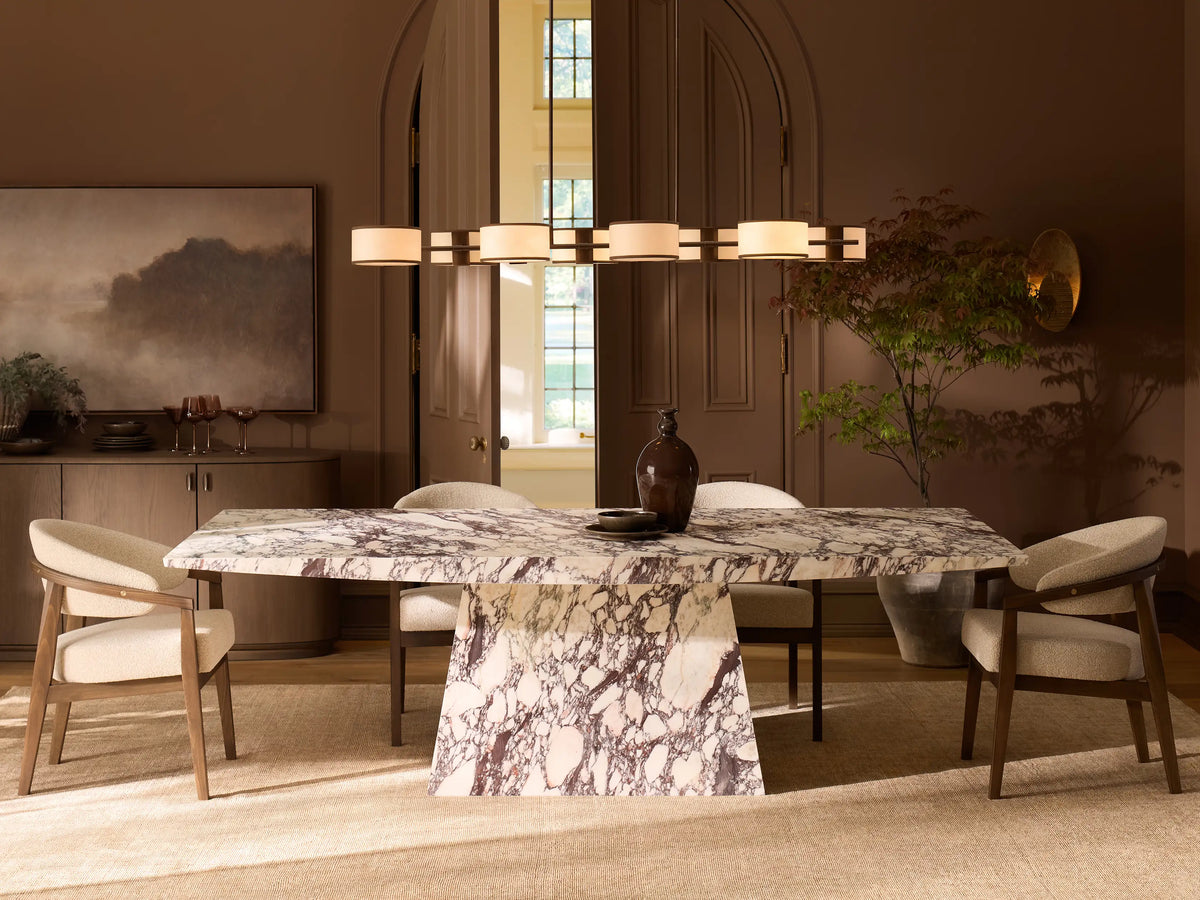 Front view of the Ilaria Dining Table, a rectangular white marble table with dark purple and brown natural veining, on a trapezoidal base.
