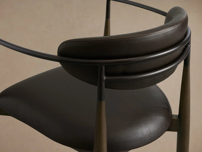 Jagger Faux Leather Dining Arm Chair in Cinder with a rounded backrest, cushioned seat, and oil-rubbed bronze frame on a wooden floor.