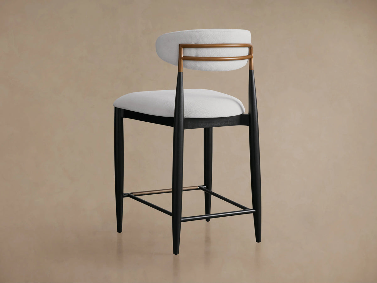 Jagger Armless Stool with a white cushioned seat and backrest, black tapered legs, and a footrest bar, on a wooden floor.