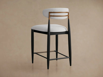 Jagger Armless Stool with a white cushioned seat and backrest, black tapered legs, and a footrest bar, on a wooden floor.