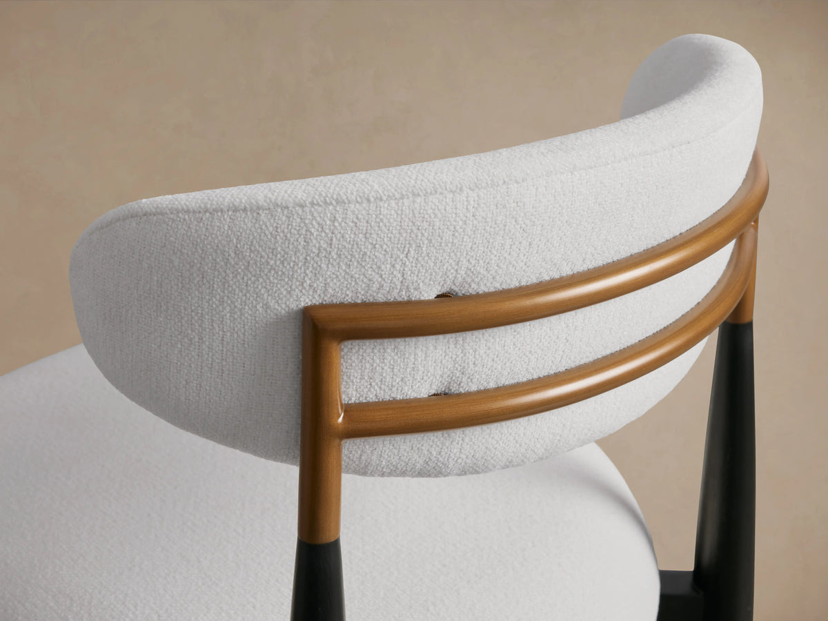 Jagger Armless Stool with white cushioned seat and backrest, black legs, on wooden floor, against a neutral wall.