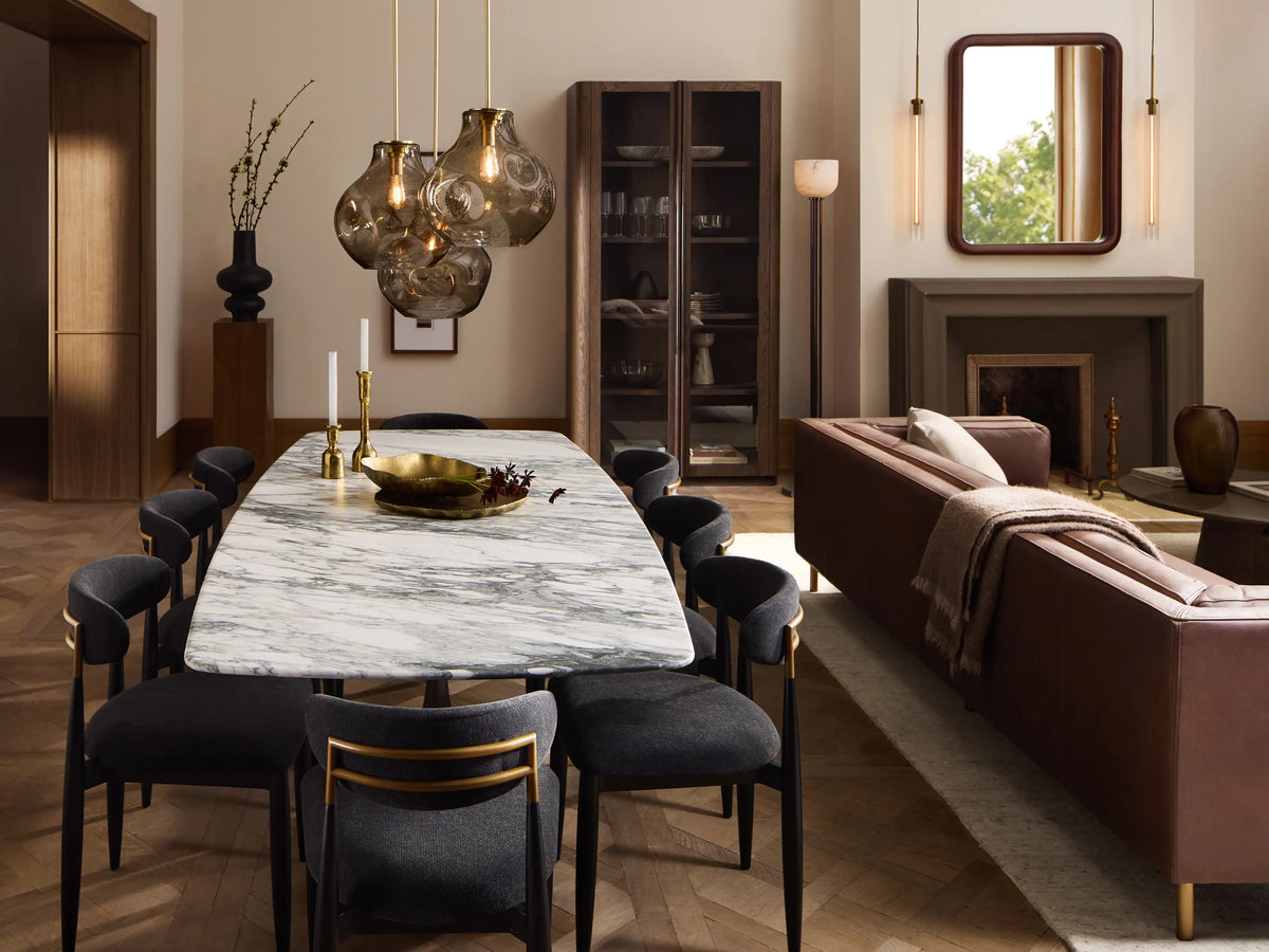 Jagger Dining Side Chair, angled, with black frame, light beige upholstered seat & curved back, gold accent, on wood floor.