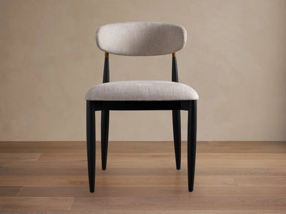Jagger Dining Side Chair: front view, light gray upholstered seat & back, black wooden frame with small gold detail.