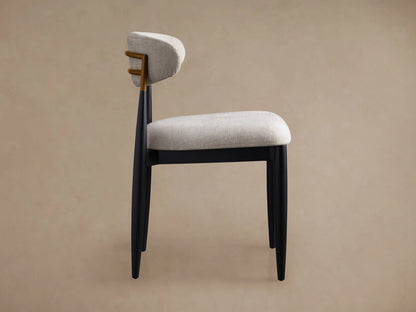 Jagger Dining Side Chair: side view. Light gray upholstered seat & curved back, dark wood frame with golden accent.