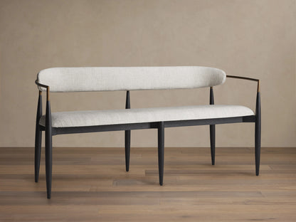 Jagger Dining Bench with a sleek design, featuring a cushioned seat and backrest in gray fabric, with black legs and golden armrests.