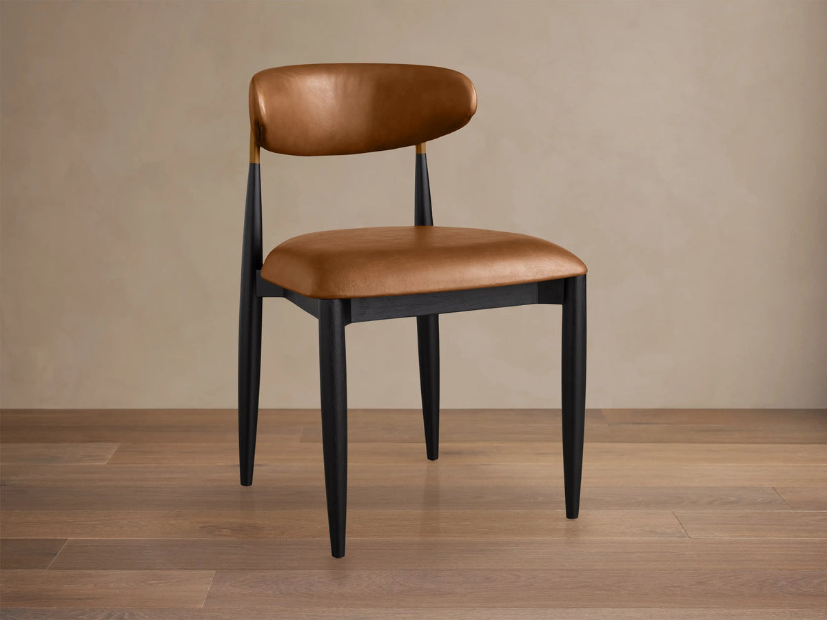 Jagger Faux Leather Dining Side Chair: Tan faux leather seat & back, sleek black frame with brass detail, on wood floor.