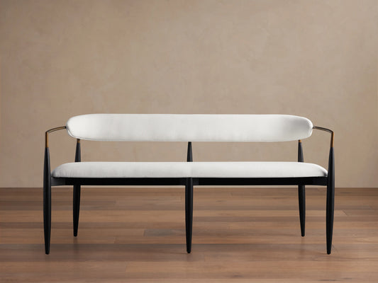 Jagger Dining Bench with white cushioned seat and backrest, black metal frame, on a wooden floor against a beige wall.