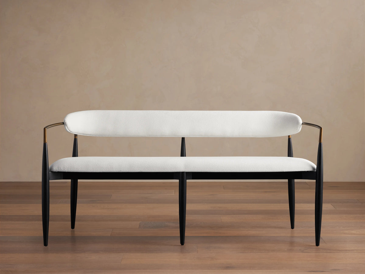 Jagger Dining Bench with a sleek black frame and white cushioned seat and backrest. It has a modern design with slender legs and gentle curves.
