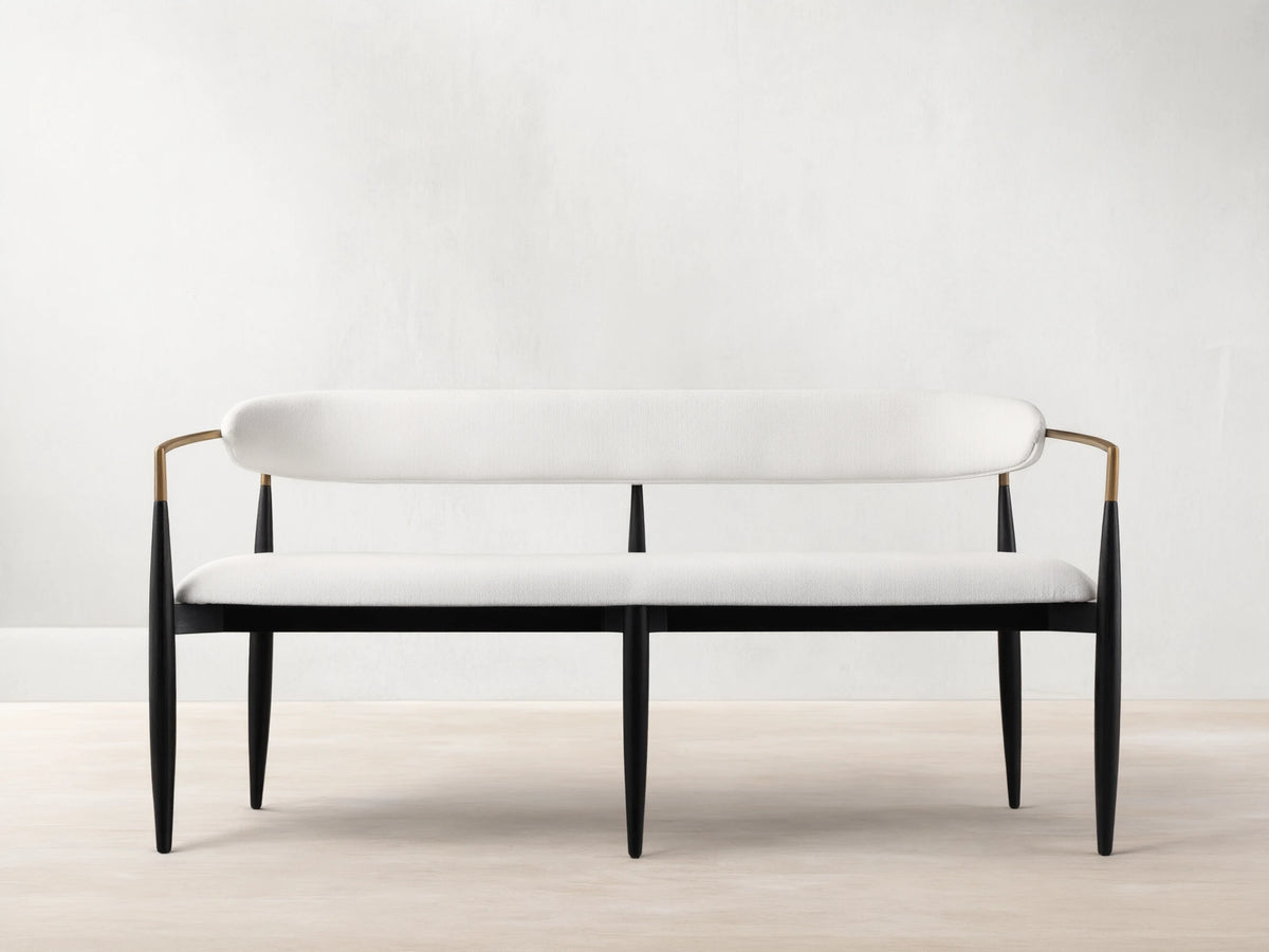Jagger Dining Bench with white cushioned seat and backrest, black metal frame, on a wooden floor against a beige wall.