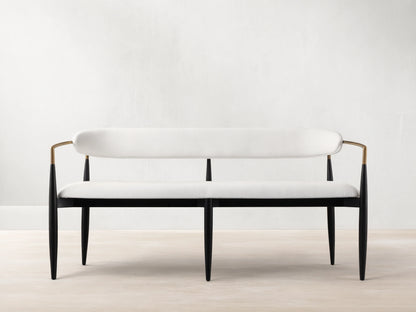 Jagger Dining Bench with white cushioned seat and backrest, black metal frame, on a wooden floor against a beige wall.