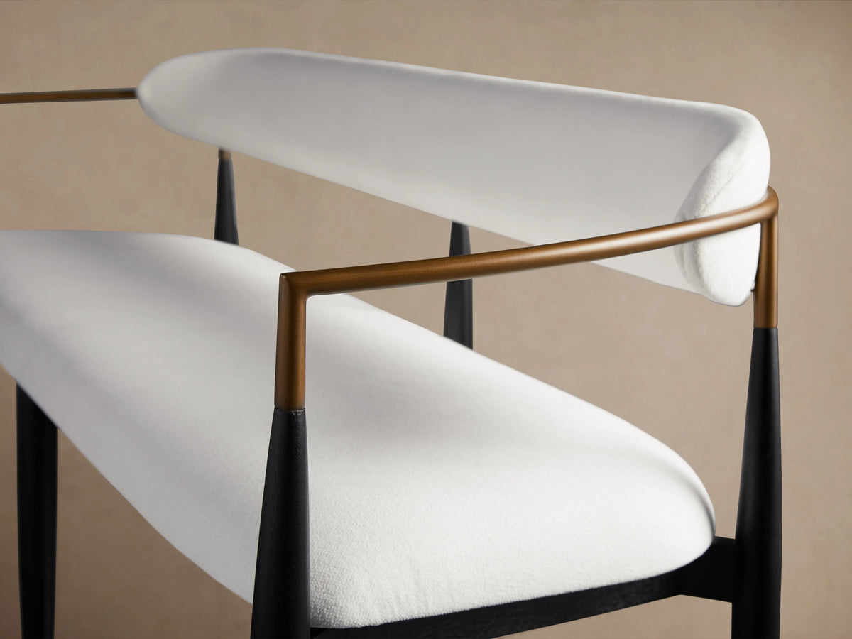Jagger Dining Bench with white cushioned seat and backrest. Bronze metal armrests, black legs. Minimalist design, side view.