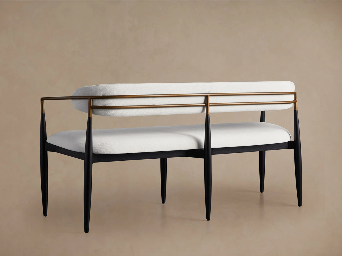 Jagger Dining Bench featuring soft white cushioned seat and backrest with bronze armrests, supported by black legs on a beige background.