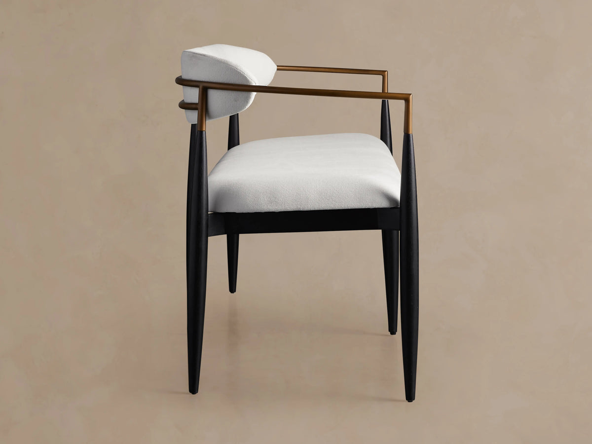 Jagger Dining Bench with white cushioned seat and back, slim black legs, and bronze side rails, on a beige background.