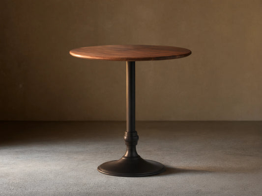 Jacob Bar Table with Wade Base, featuring a round walnut tabletop and a sleek black iron base, set on a wooden floor.