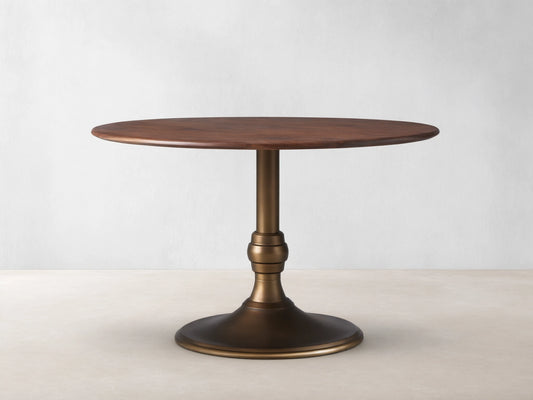 Jacob Bistro Table with a warm walnut round tabletop, supported by an elegant brass-finished Wade Base on a wooden floor.