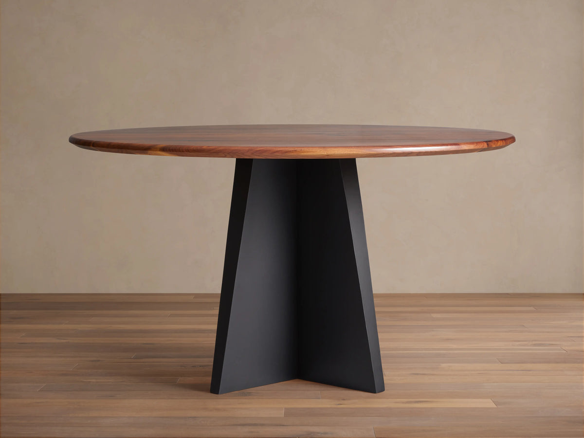 Jacob Round Dining Table with a dark brown walnut top & black geometric Vertex base, shown centered on a wood floor.