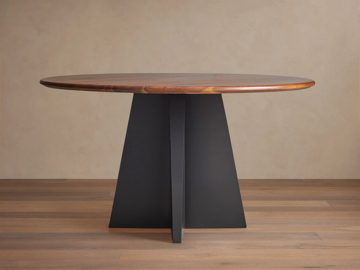 Jacob Round Dining Table with a dark brown walnut top & black geometric Vertex base, shown centered on a wood floor.