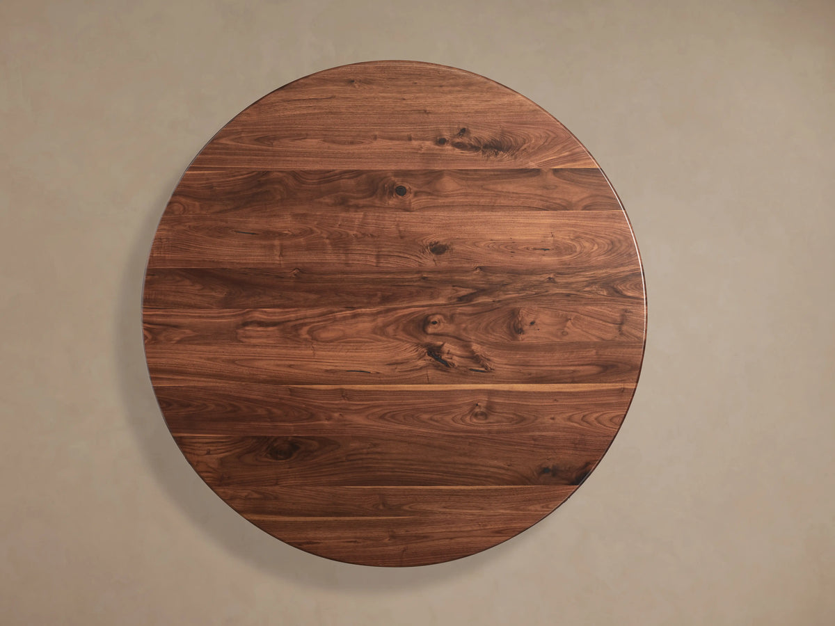 Angled close-up of Jacob Round Dining Table's dark walnut wood tabletop, showcasing its rich grain and smooth, reflective surface.