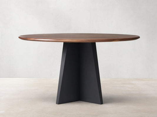 Jacob Round Dining Table with a dark brown walnut top & black geometric Vertex base, shown centered on a wood floor.