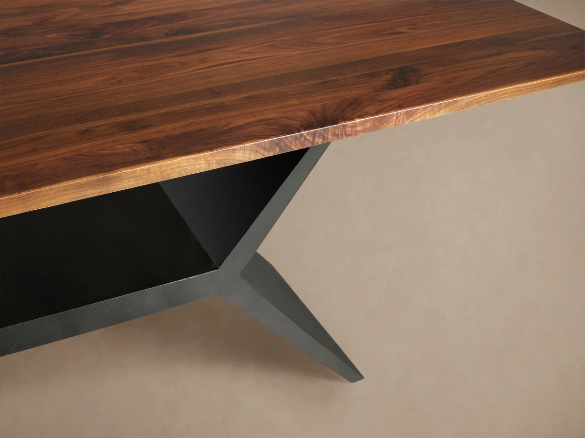 Jacob Dining Table: rectangular dark brown walnut top with reddish edges, black angular vertex base, angled view on neutral background.