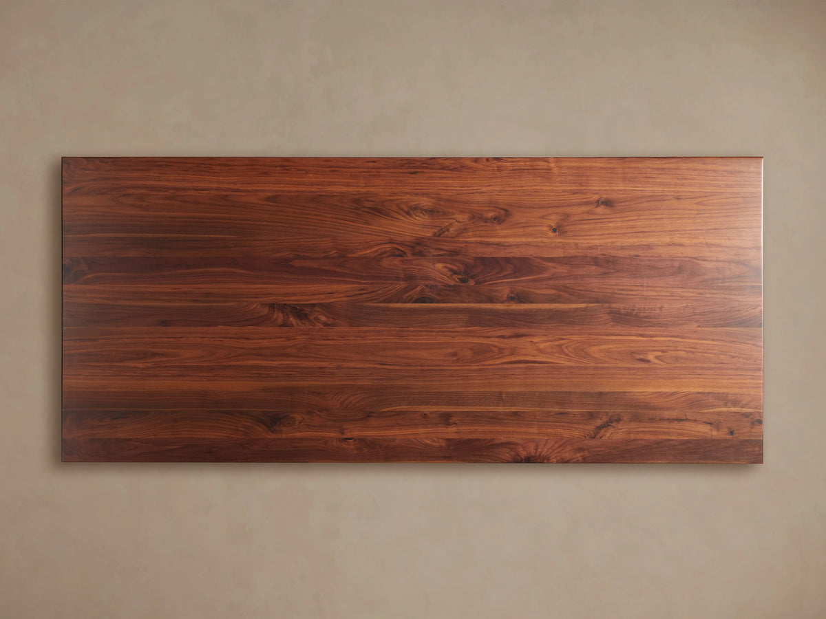 Jacob Dining Table with a rich brown walnut wood top, showing natural grain, and a dark gray angular vertex base.