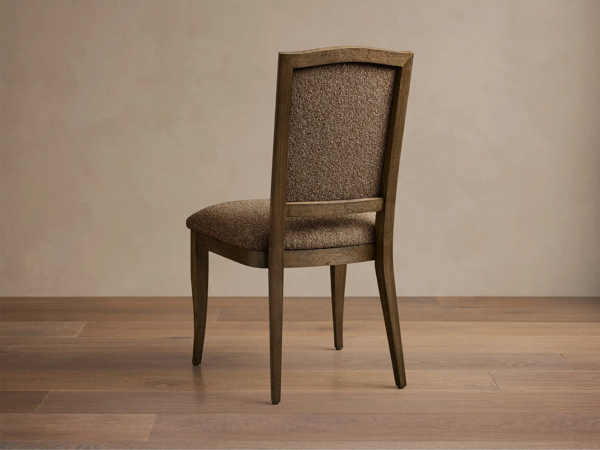 Close-up of the light brown textured upholstery and visible oak frame on the Jeannine Upholstered Camel Back Dining Side Chair.