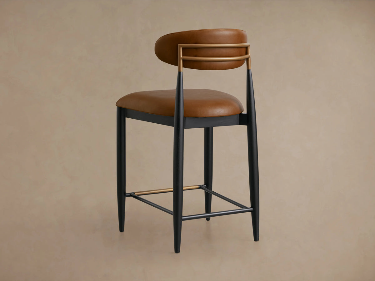 Jagger Faux Leather Armless Stool with brown faux leather seat and backrest, black frame and legs, on wooden floor.