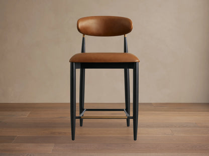 Jagger Faux Leather Armless Stool with brown faux leather seat and back. Black metal frame with gold accents and footrest.